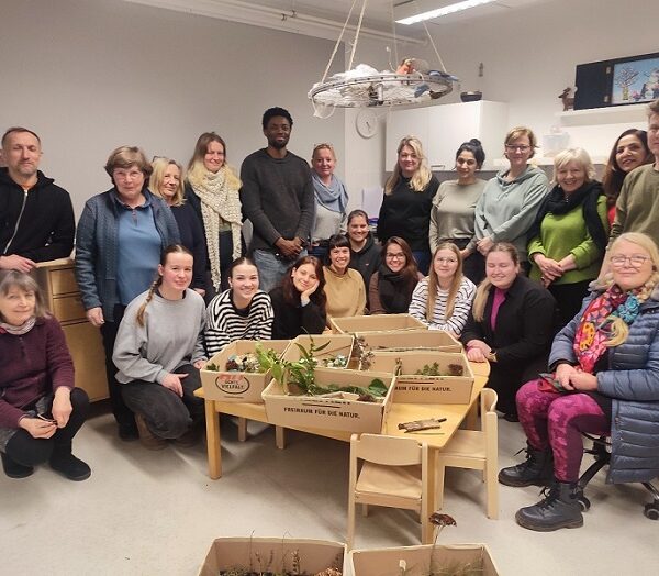 Eine Gruppe Menschen gestaltet zusammen einen Workshop zur Gestaltung des Außengeländes eines naturnahen Kindergartens.