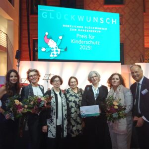 Die Preisträger und Preisträgerinnen stehen zusammen vor der Bühne und freuen sich über Blumen und einen symbolischen Scheck.