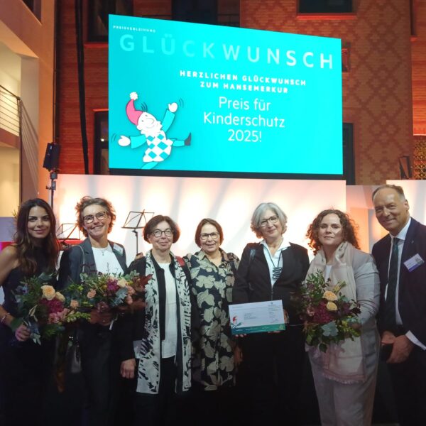 Die Preisträger und Preisträgerinnen stehen zusammen vor der Bühne und freuen sich über Blumen und einen symbolischen Scheck.