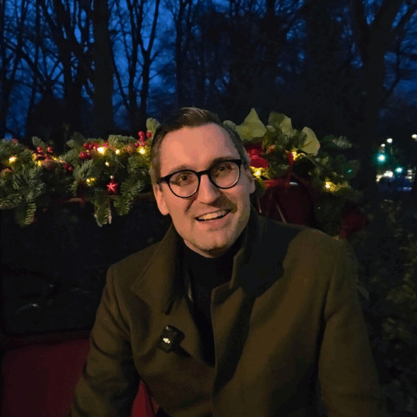 Alexander Letzel im Dunkeln vor einem mit Weihnachtslämpchen beleuchtetem Hintergrund.