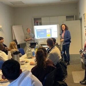 Zugewanderte Jugendlichen sitzen um einen Tisch, schauen auf eine Präsentation und werden von Experten zu Ausbildungschancen im Handwerk informiert.