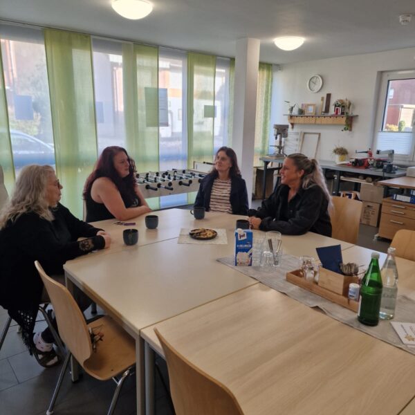 Vier Frauen sitzen bei einer Tasse Kaffee um den Tisch und sprechen miteinander.