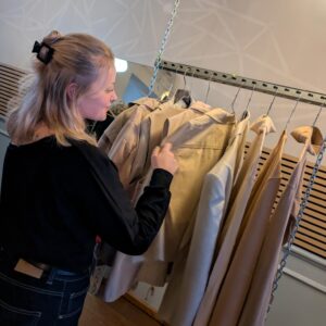 Eine Frau stöbert durch eine Kleiderstange mit sortierter Kleidung beim Stoffmarkt.