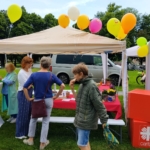 Der Pavillon und Infostand sind mit bunten Luftballons dekoriert. Vor dem Infostand und am Stehtisch nebendran werden intensive Gespräche geführt.