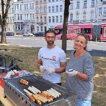 Hüseyin Kizmaz und Michaela Hamacher stehen am Grill und grillen Würstchen.