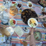 Eine gut gedeckte Picknickdecke mit Platten voll gegrilltem Fleisch und Gemüse