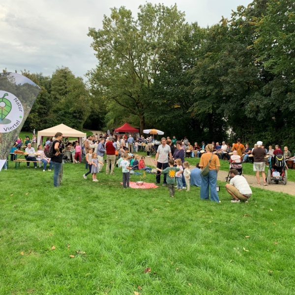 Viele Menschen stehen und sitzen auf einer Wiese.