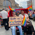 Zwei Frauen sitzen im Flaniermobil und halten ein Schild mit der Aufschrift "Kinder von Regenbogenfamilien gleichstellen".